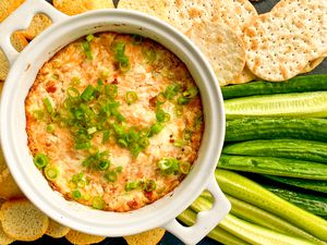 Overhead view of 3-ingredient smoked salmon dip in a white bowl topped green onions and surrounded by crackers, baguette slices and sliced cucumbers