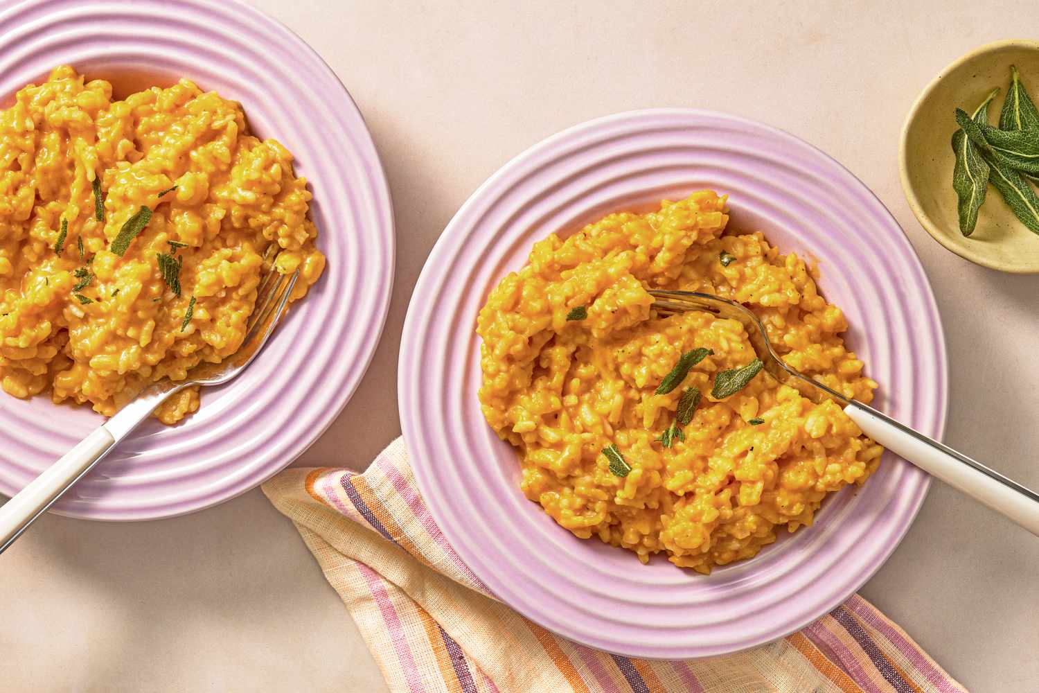 Two bowls of risotto with garnishes served with spoons and a striped napkin