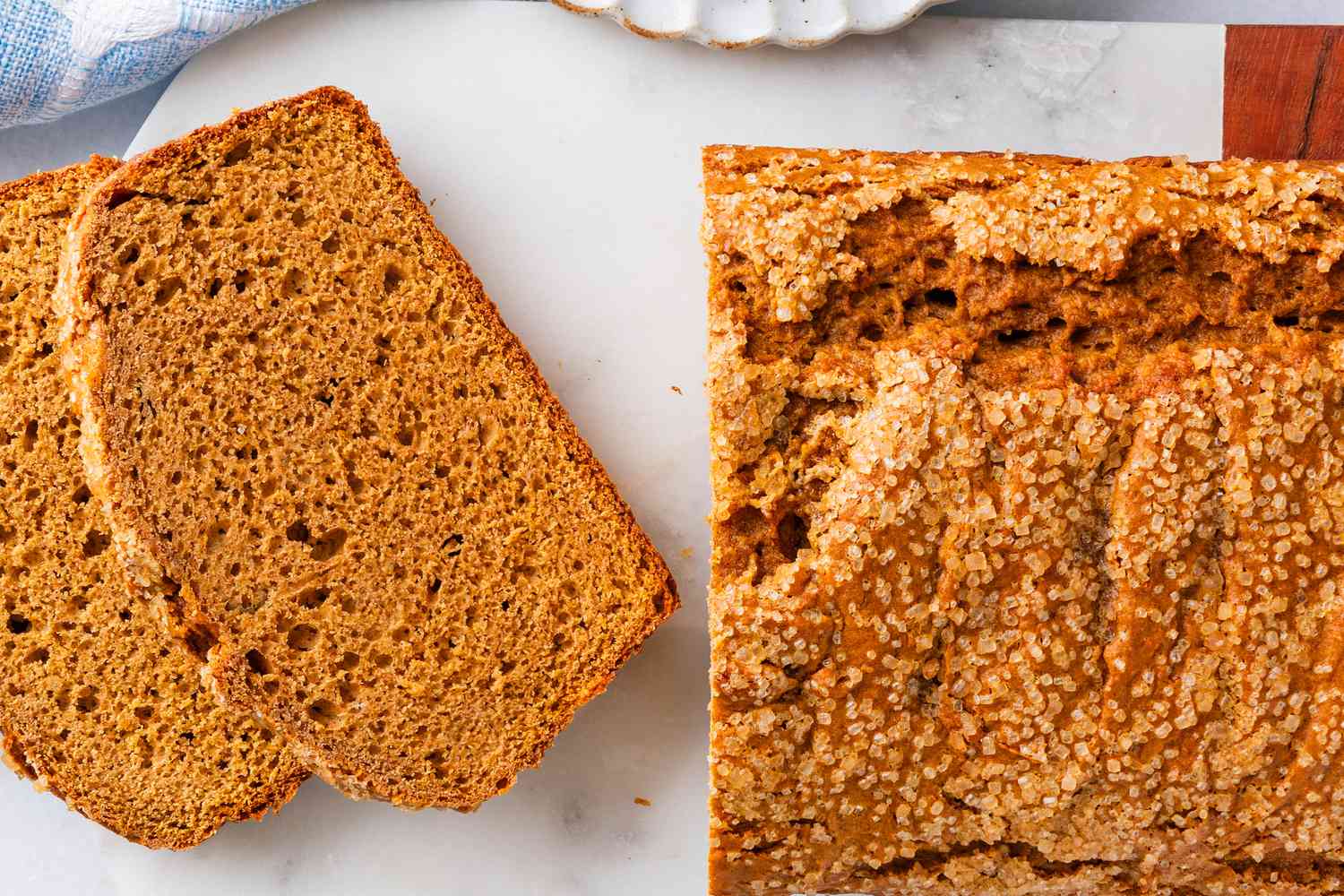 Overhead view of a loaf of pumpkin bread on a marble cutting board with two slices in front