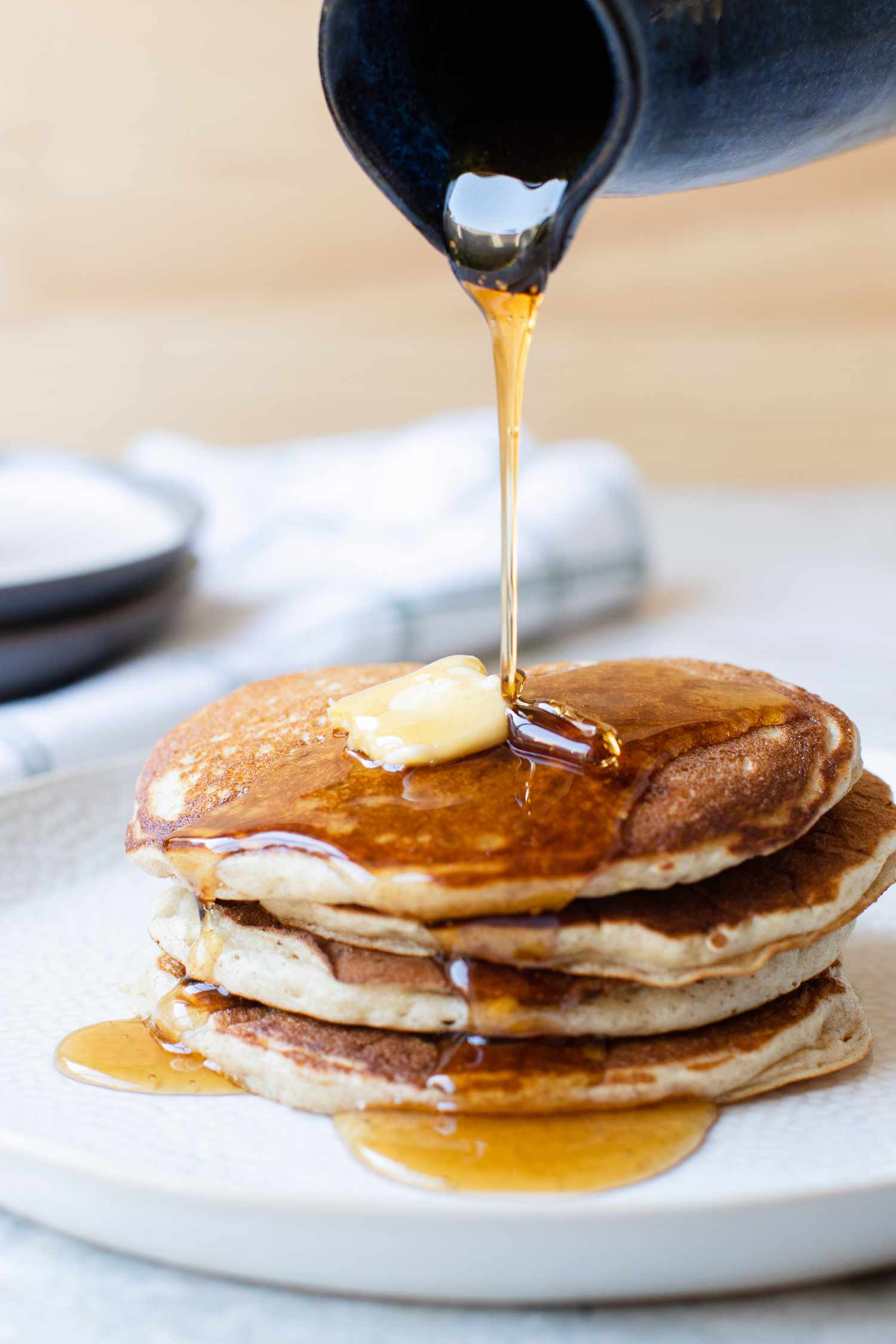 Stack of Buckwheat Pancakes Topped with Maple Syrup and Some Butter, and Next to It, a Glass of Milk and a Container of More Syrup