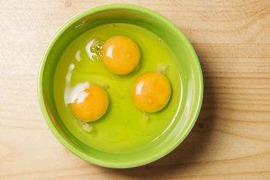 A top-down image of a green bowl filled with three raw eggs.