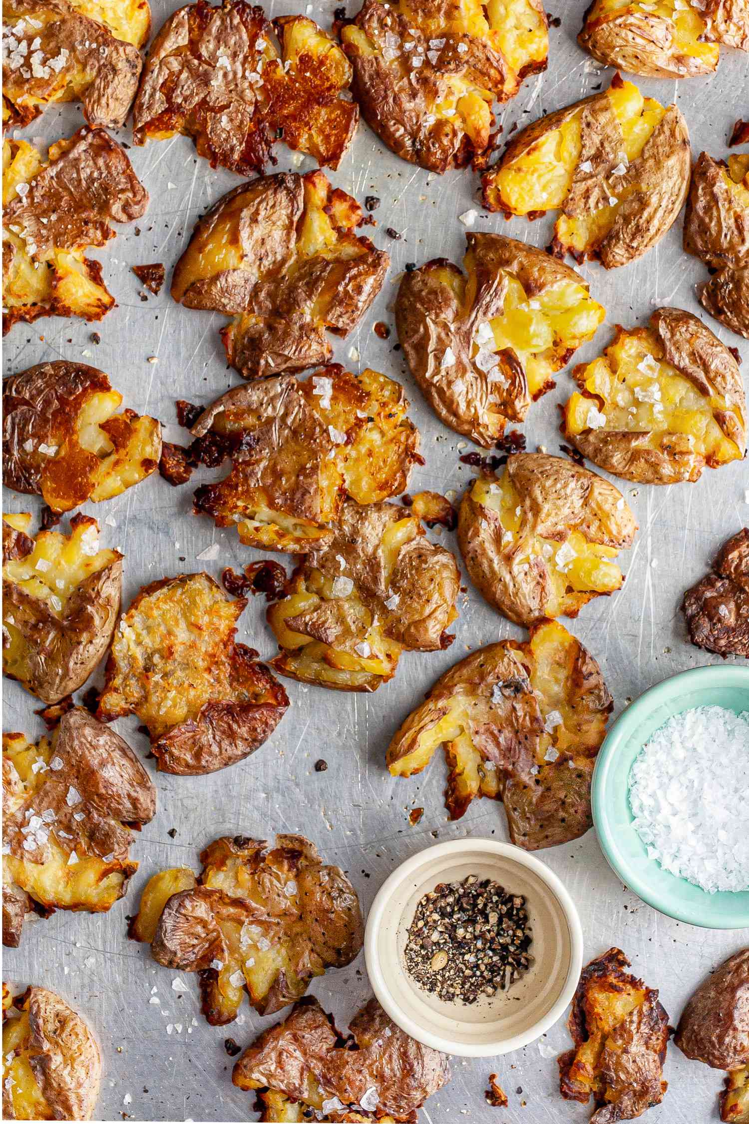 Smashed Potatoes and Two Small Bowls (One with Cracked Pepper and Another with Flaky Salt) on a Baking Pan 