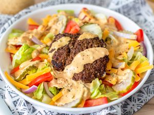 Bowl of Burger Salad Topped With a Hefty Drizzle of Dressing, Sitting on a Table Napkin