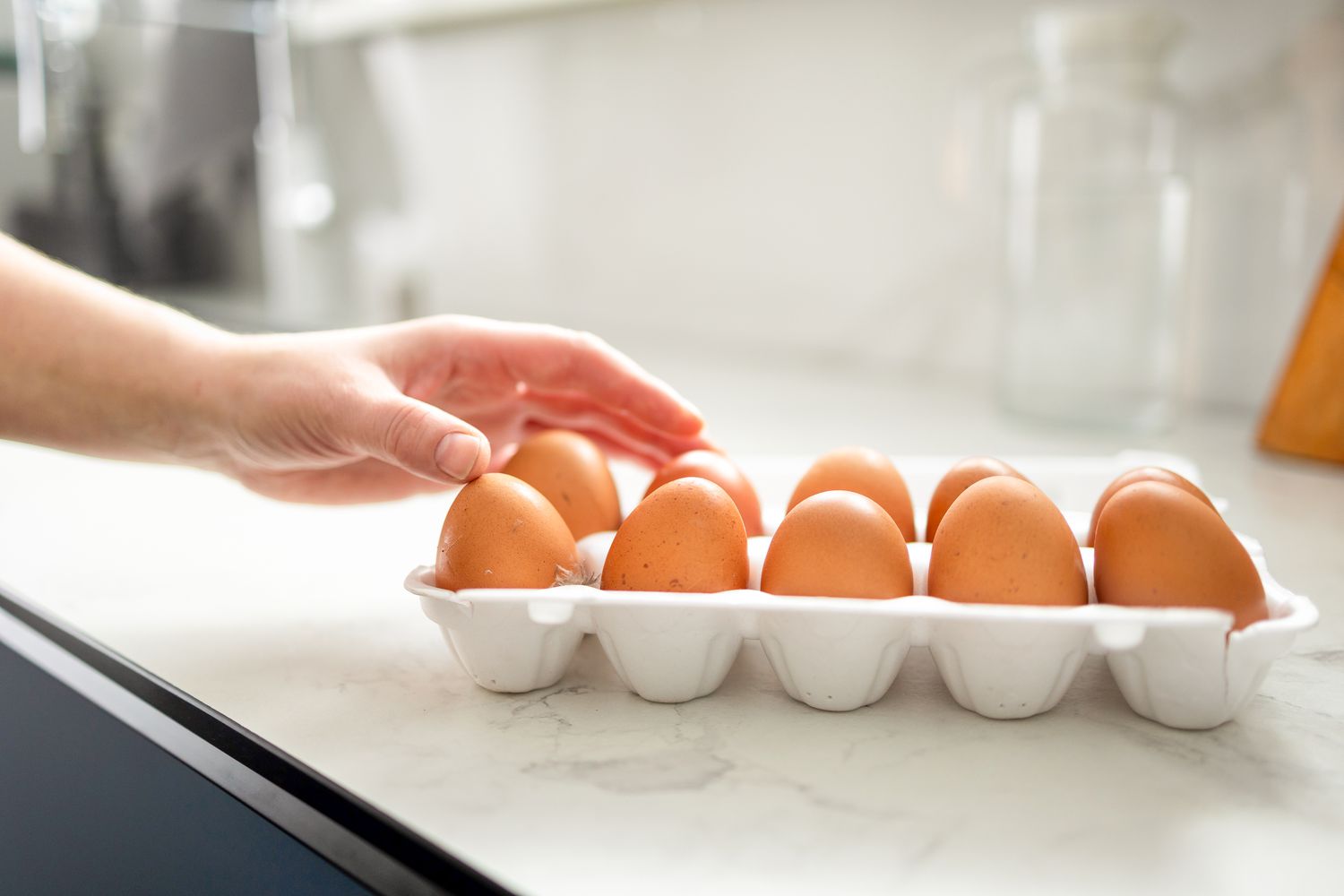Hand reaching toward eggs in a carton on a countertop