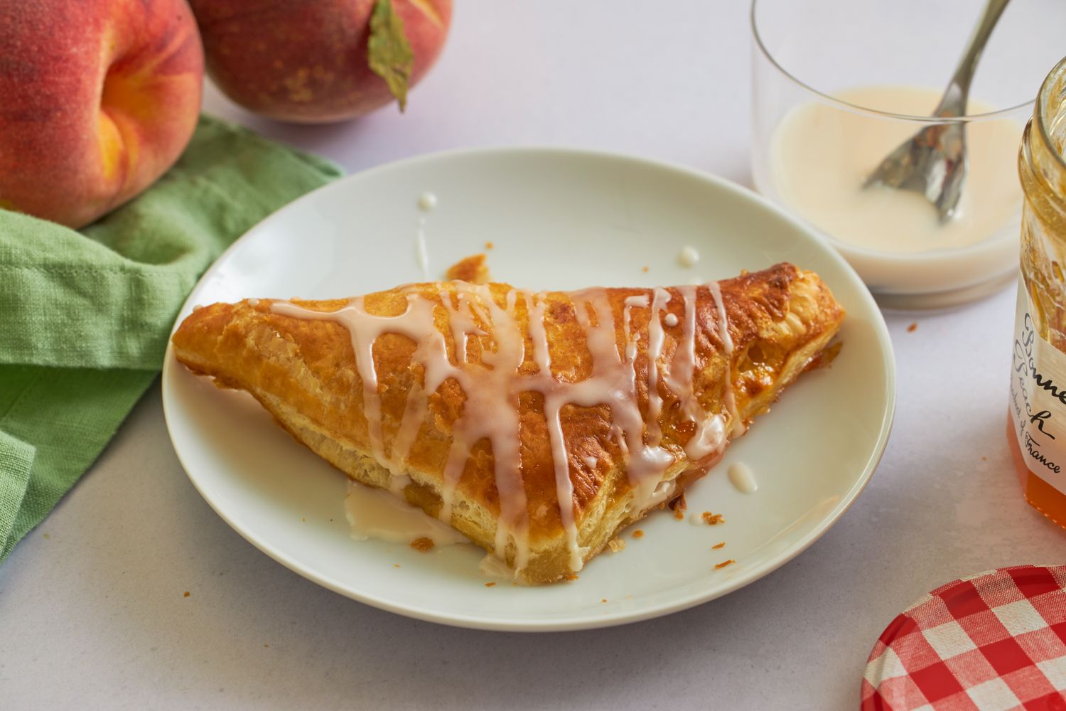 Peach turnover on a plate glazed with icing next to peaches and a jar of jam
