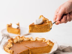 Slice of Old Fashioned Pumpkin Pie Held on a Pie Server with the Rest in a Pie Dish Below It 