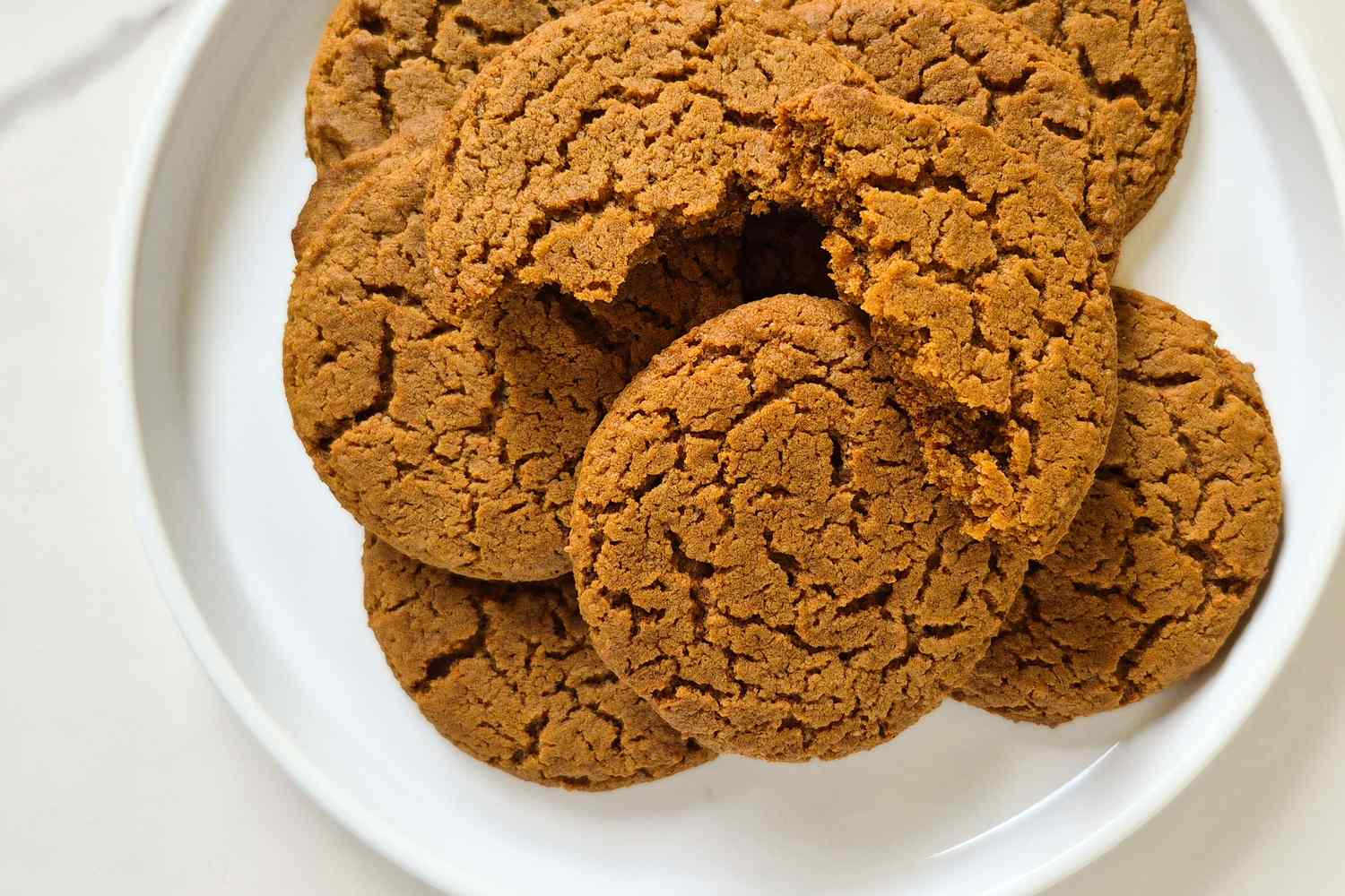 Round ginger cookies arranged on a white plate one cookie slightly broken near the center