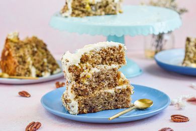 Side view of a blue plate with a tall slice of southern hummingbird cake and a cake on a cake stand behind it.