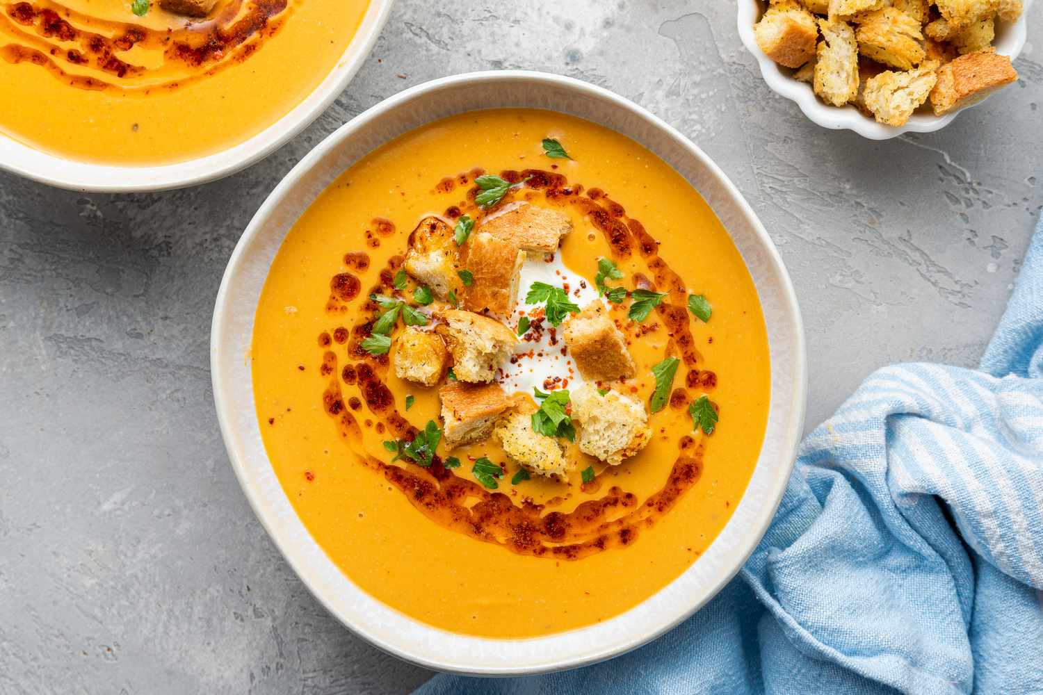 Overhead view of a bowl of creamy soup garnished with croutons and oil