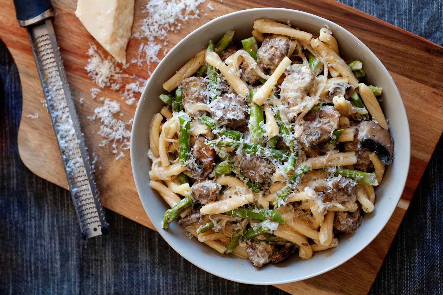 Pasta with mustard sauce, Italian sausage, and asparagus in a bowl and topped with shredded parmesan.