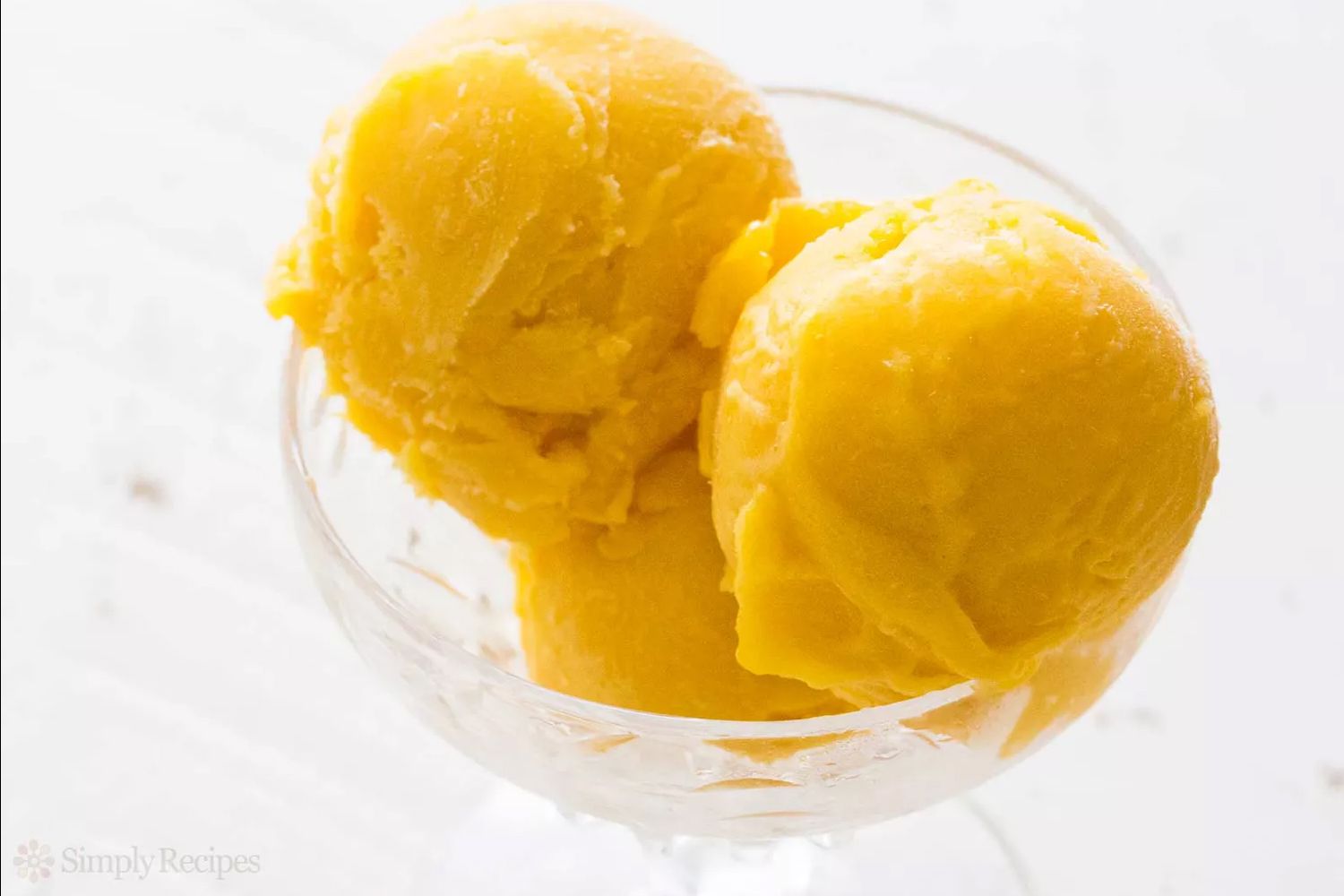 Two scoops of yellow frozen dessert in a glass dish