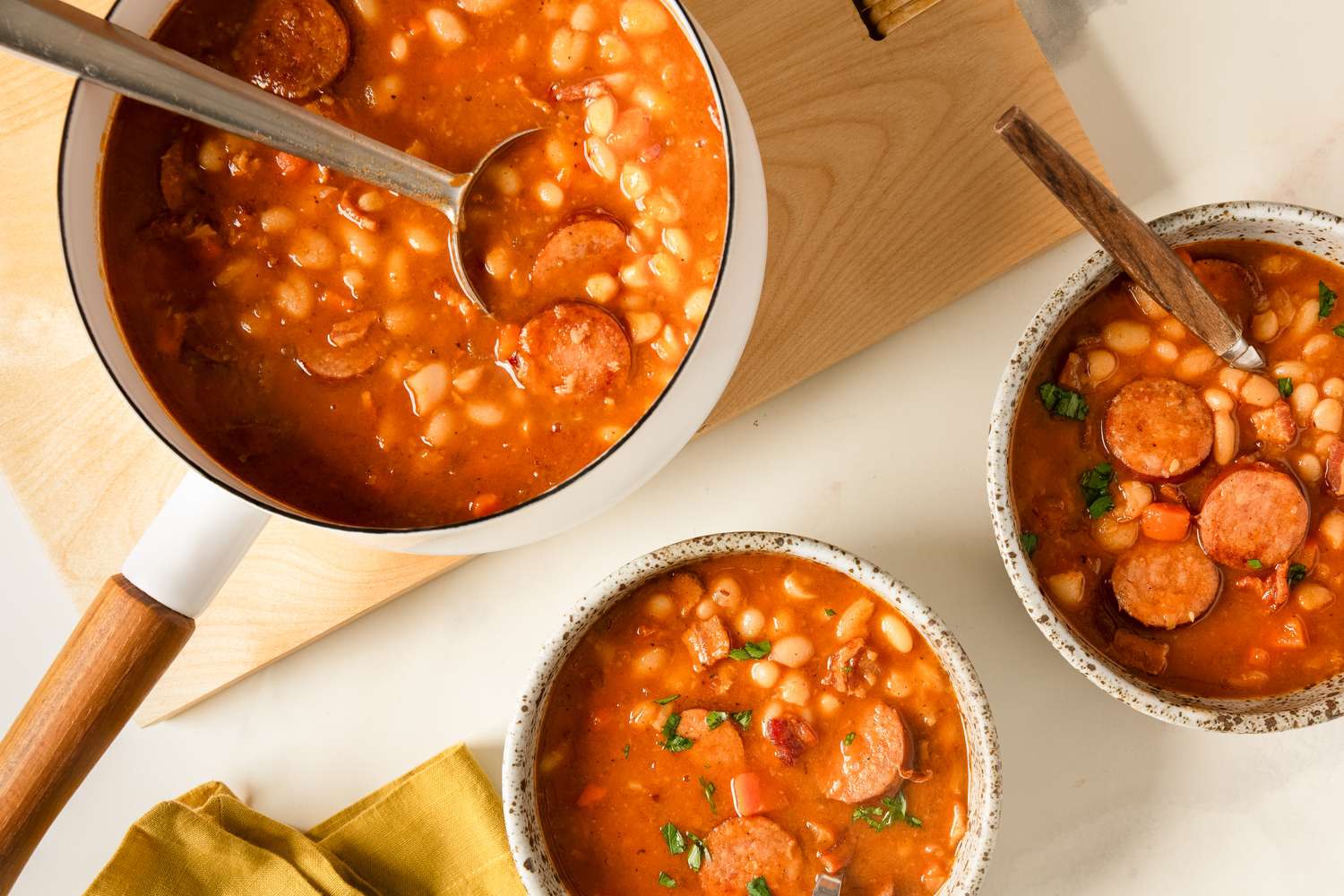 Bowls of bean and sausage soup served with a serving pot and spoon