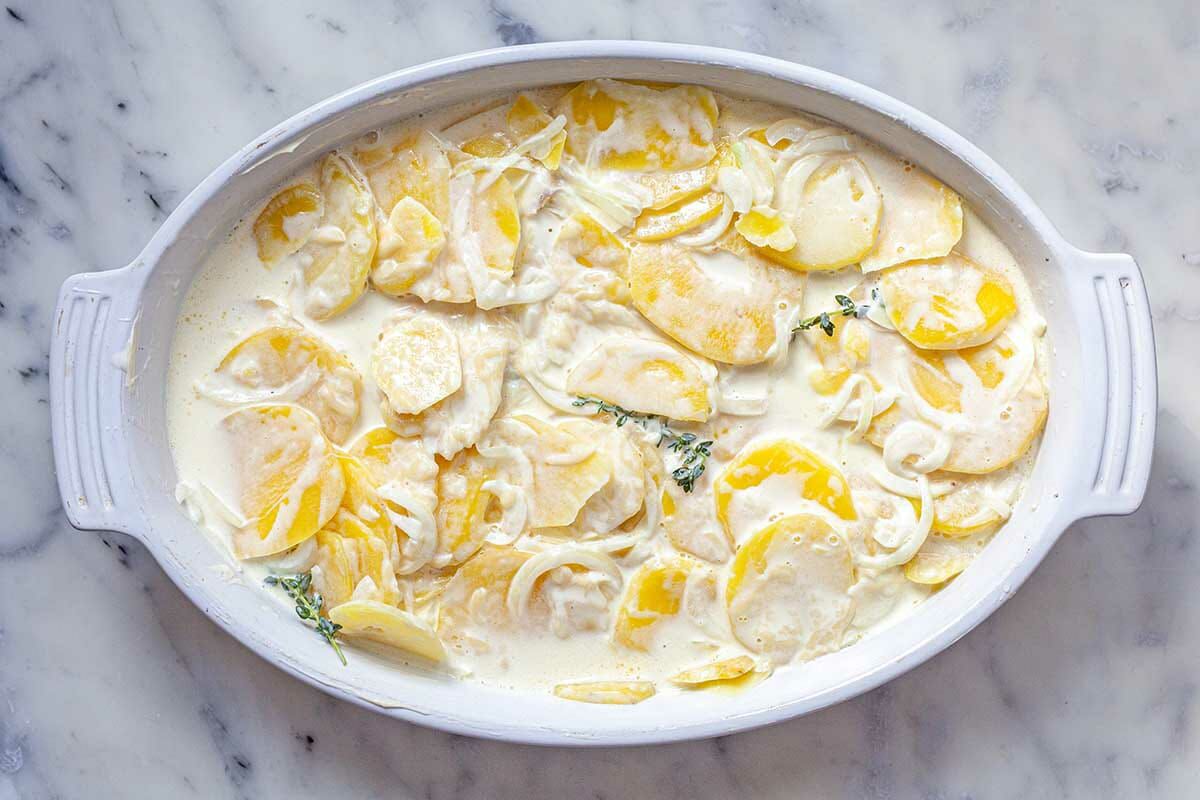Au Gratin Potatoes covered in a cream sauce in an oval ceramic casserole dish.