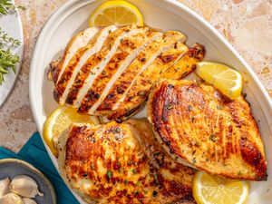 Marinated chicken breasts on a white platter with lemon slices