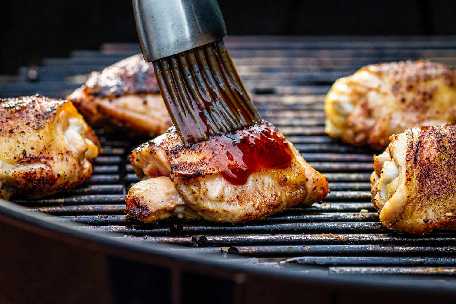 Basting chicken thighs with BBQ sauce on a charcoal grill