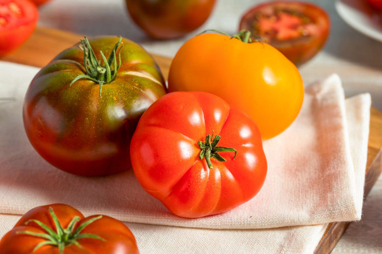 heirloom tomatoes (various colors) on a kitchen towel surrounded by more heirloom tomatoes (some cut in half)
