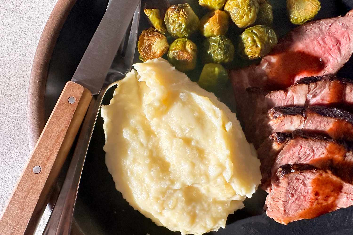 A plate showing mashed potatoes, steak, and Brussels sprouts