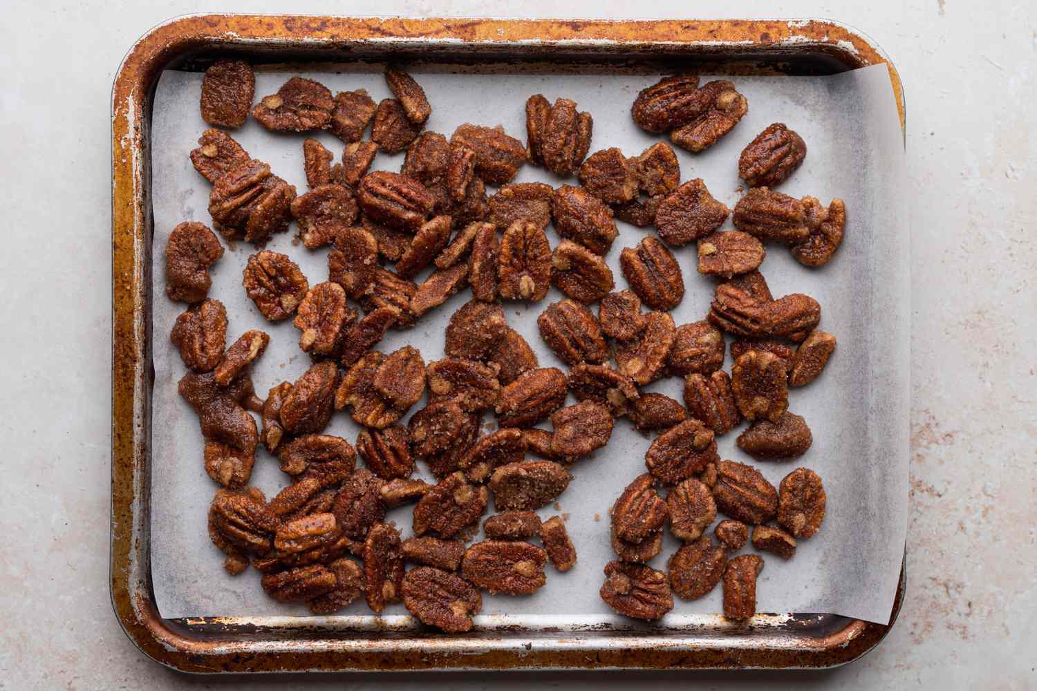 Overhead view of a baking sheet with sugared pecans spread on it.