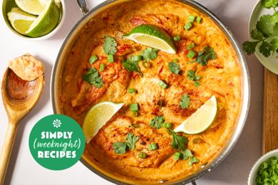 A pan of a cooked dish garnished with lime wedges herbs and sauce