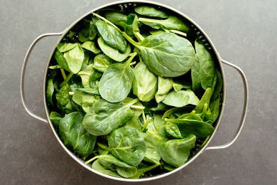 A colander filled with fresh spinach leaves