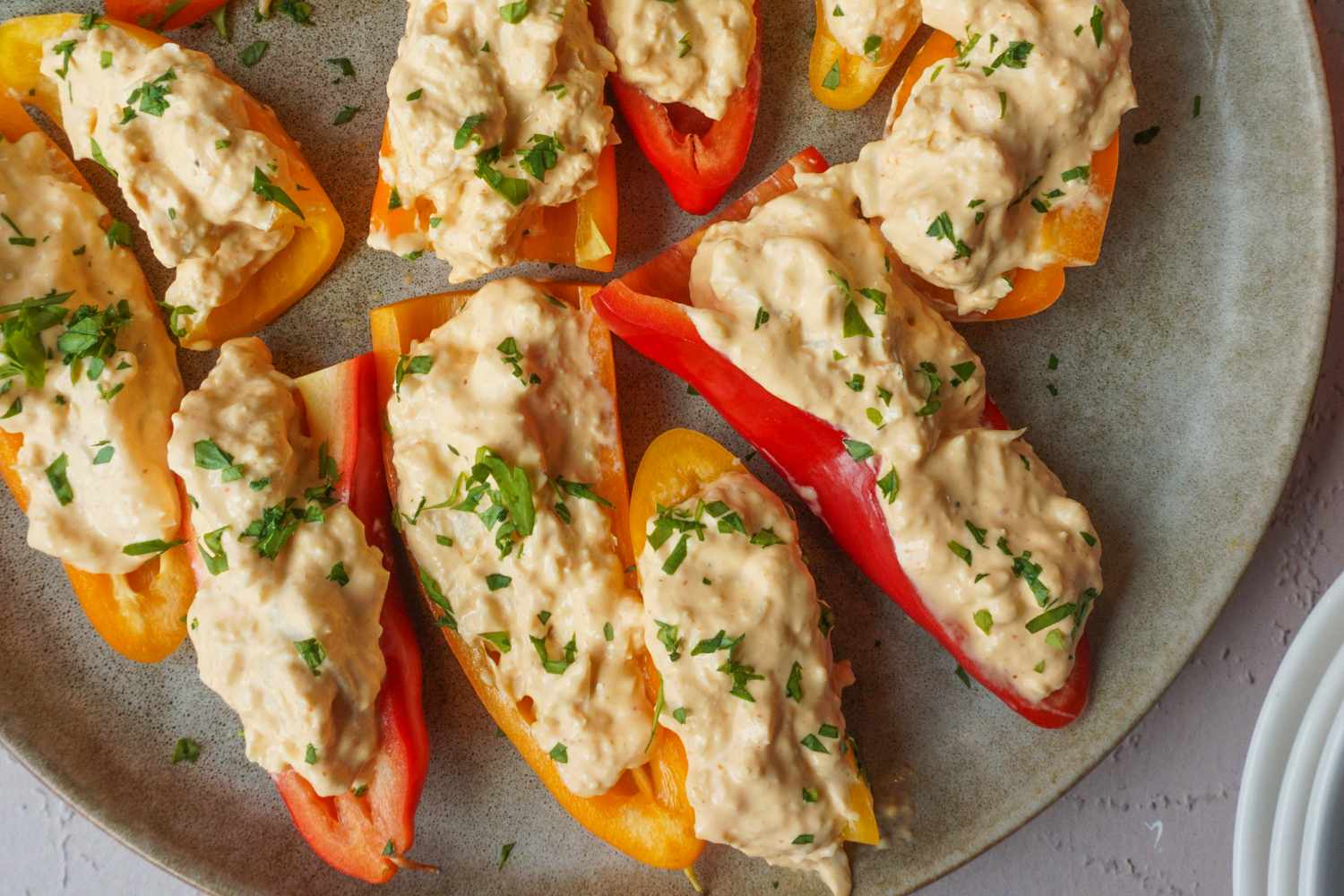 Halved mini bell peppers filled with a creamy dip and garnished with chopped herbs arranged on a plate