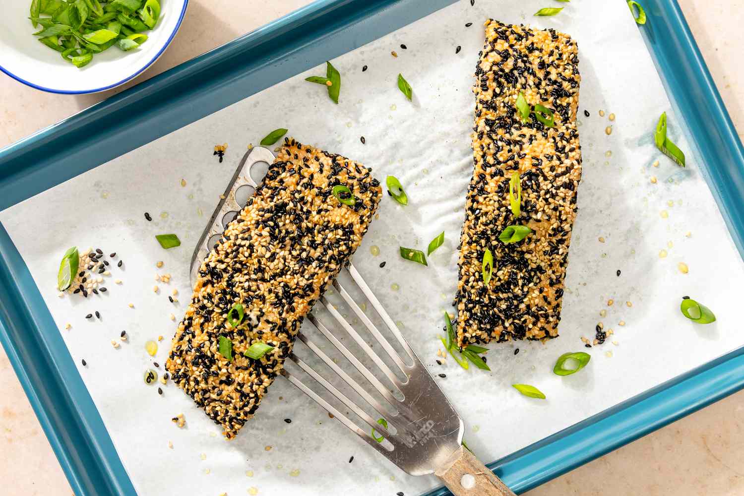 Sesame-crusted salmon fillets on a baking tray, garnished with green onions