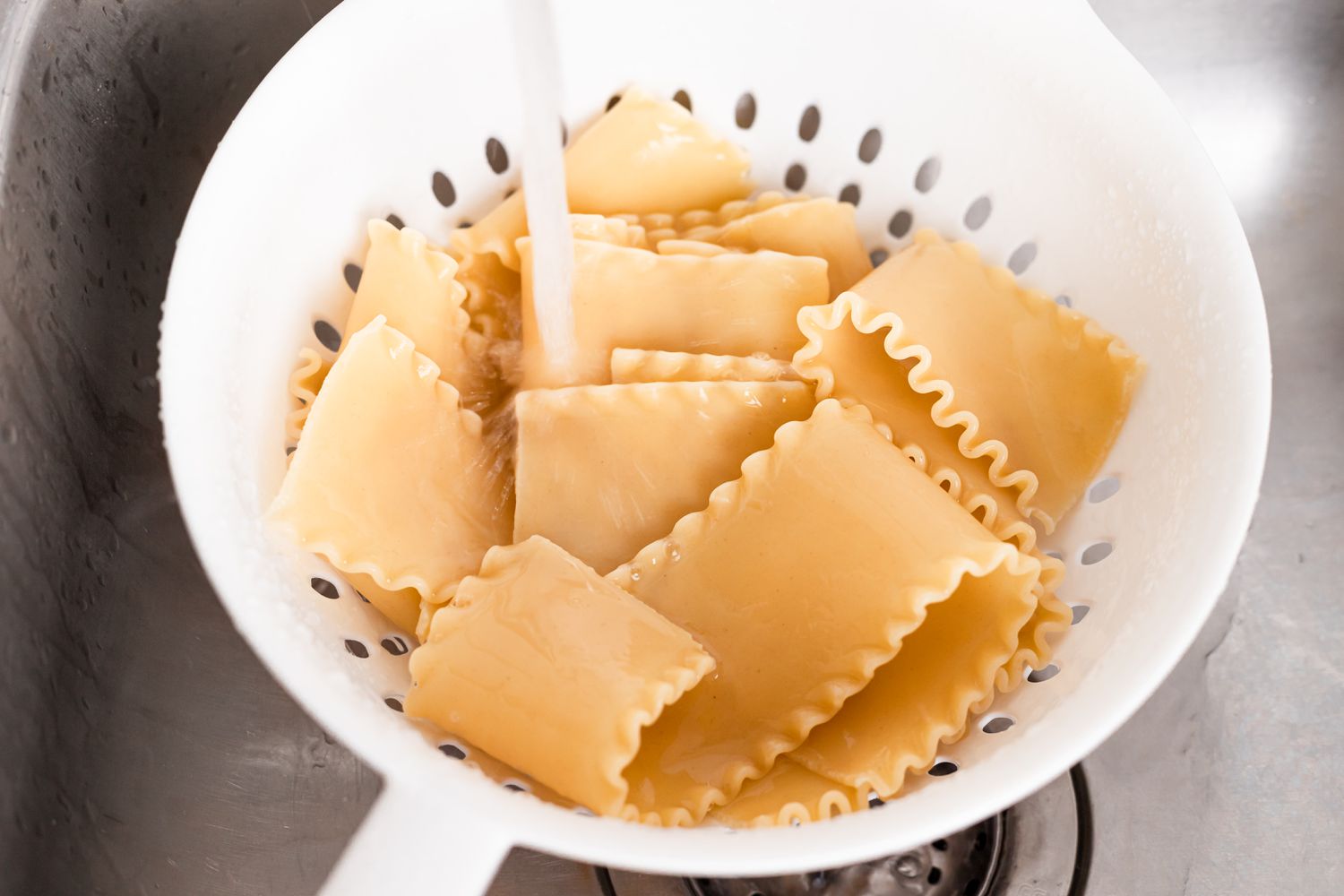 Draining noodles in a colander and running water over them for a lasagne recipe.