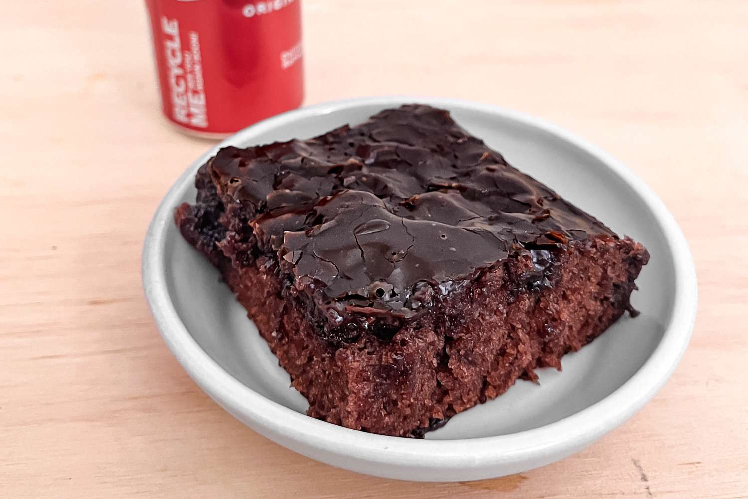 Slice of Coca Cola cake in a small bowl and a can of Coca-Cola in the background