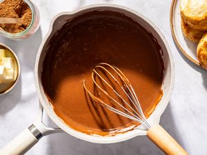 A whisk in a pot of chocolate gravy with butter and biscuits nearby