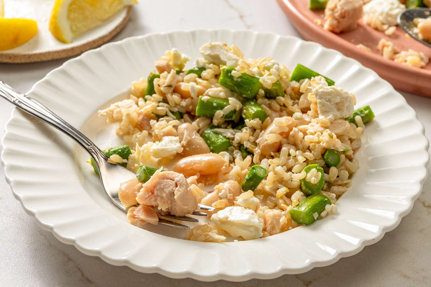Plate of brown rice mixed with asparagus, pieces of salmon, and cheese, fork on the plate