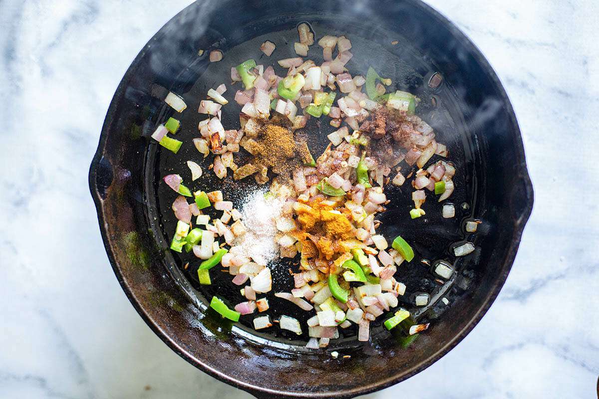 Onions, spices and jalapenos being toasted in a black skillet for vegetable samosa filling.
