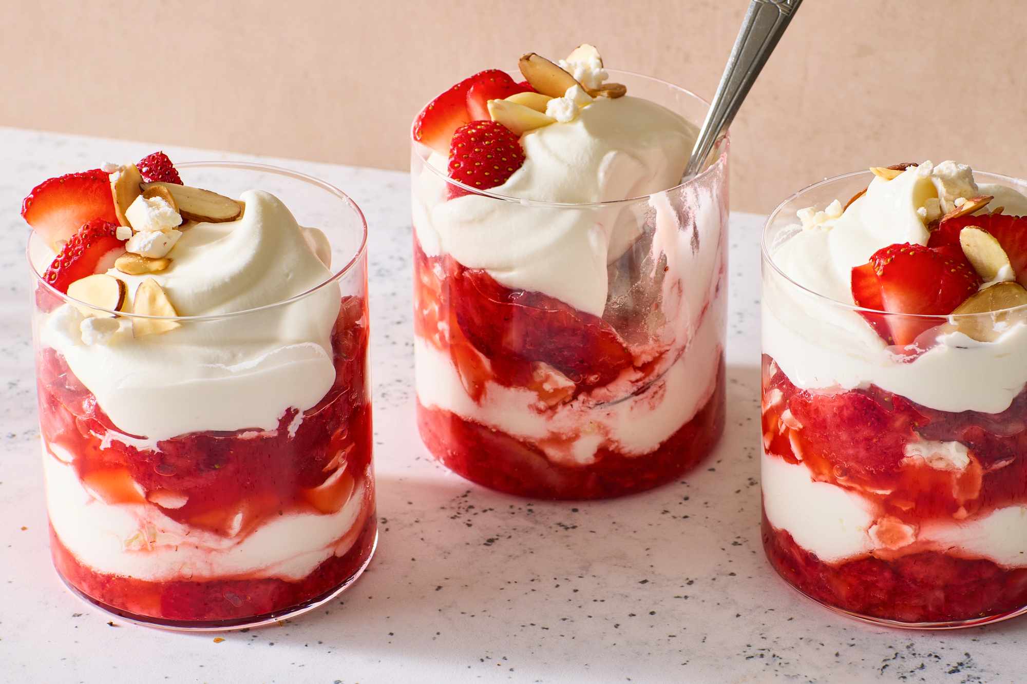 Glass desserts layered with whipped cream, strawberries, and sliced almonds
