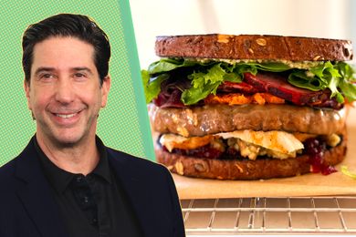David Schwimmer next to a sandwich filled with assorted ingredients placed on a wire rack