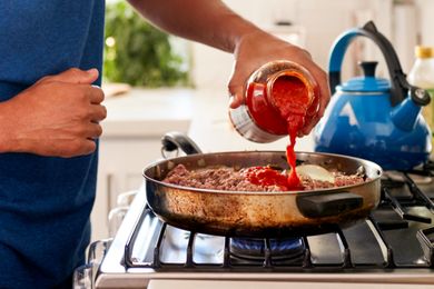 Person pouring tomato sauce into a skillet on a stove