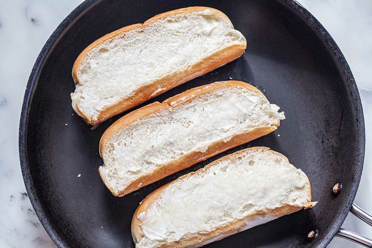 Three split rolls buttered and in a skillet to toast for a homemade lobster roll recipe.