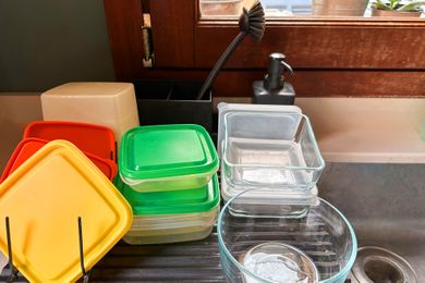 Plastic and glass food storage containers drying on a dish rack near a sink