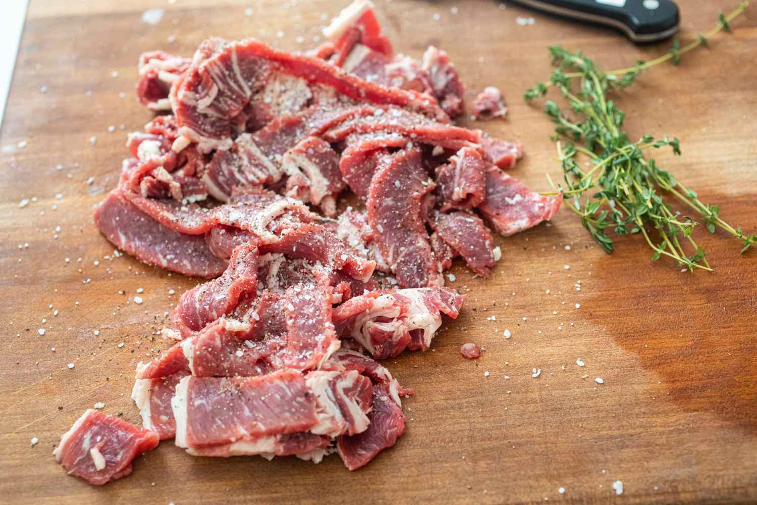 Sliced beef on a cutting board to show how to make a Philly cheese steak.