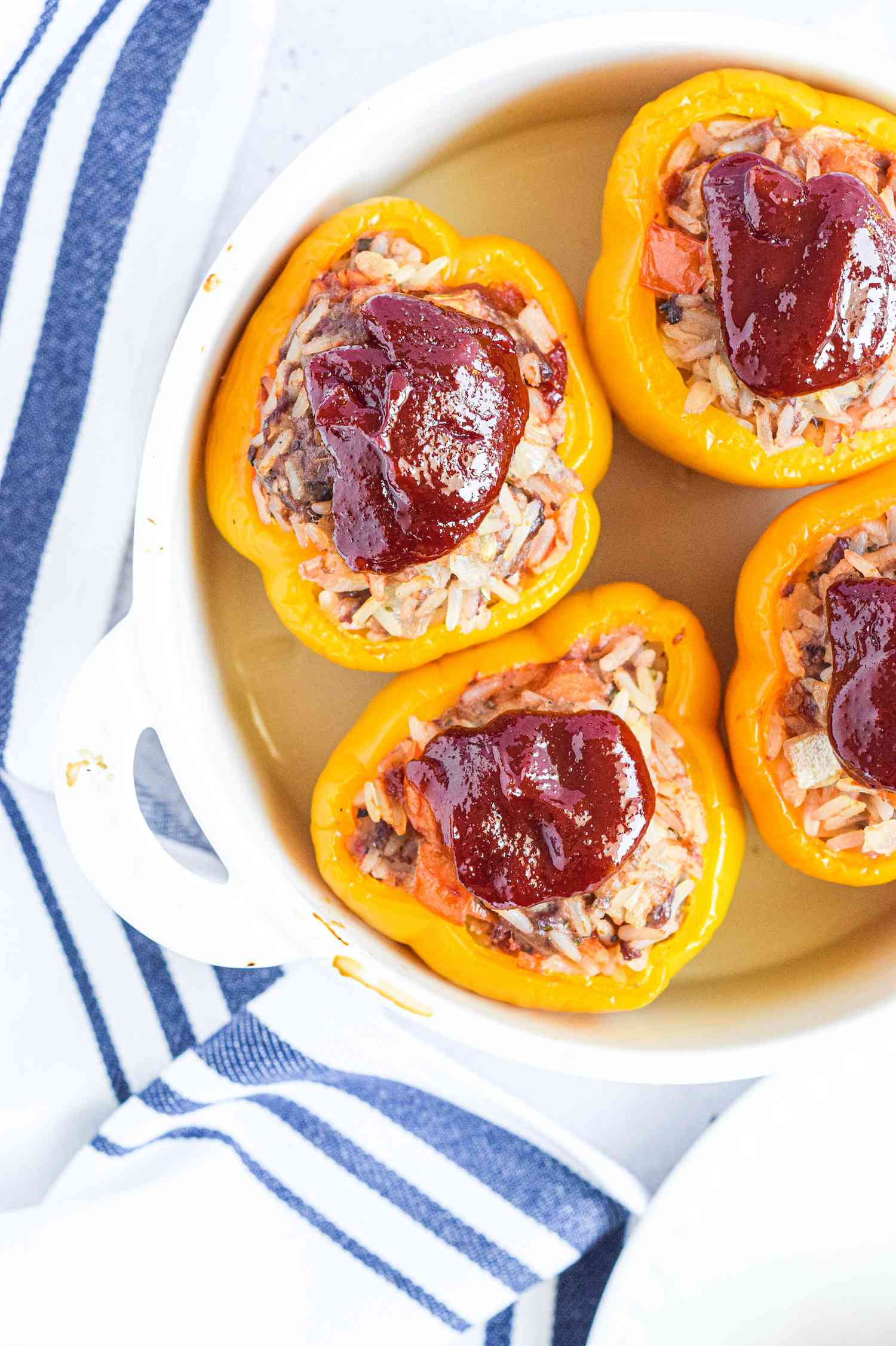 Round ceramic dish with four stuffed bell peppers inside.