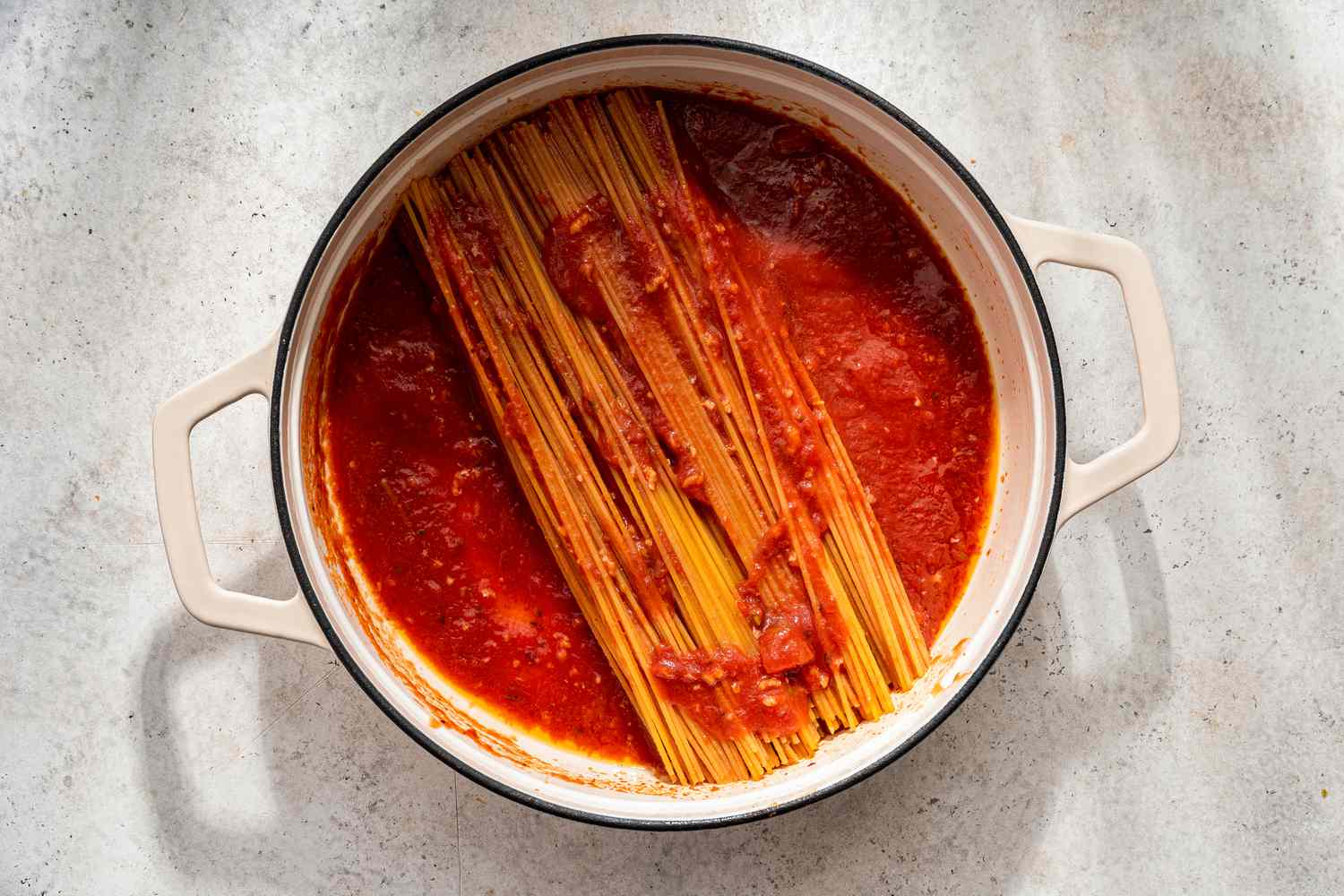 Uncooked spaghetti added to the pot and topped with a bit of sauce for assassin's spaghetti recipe