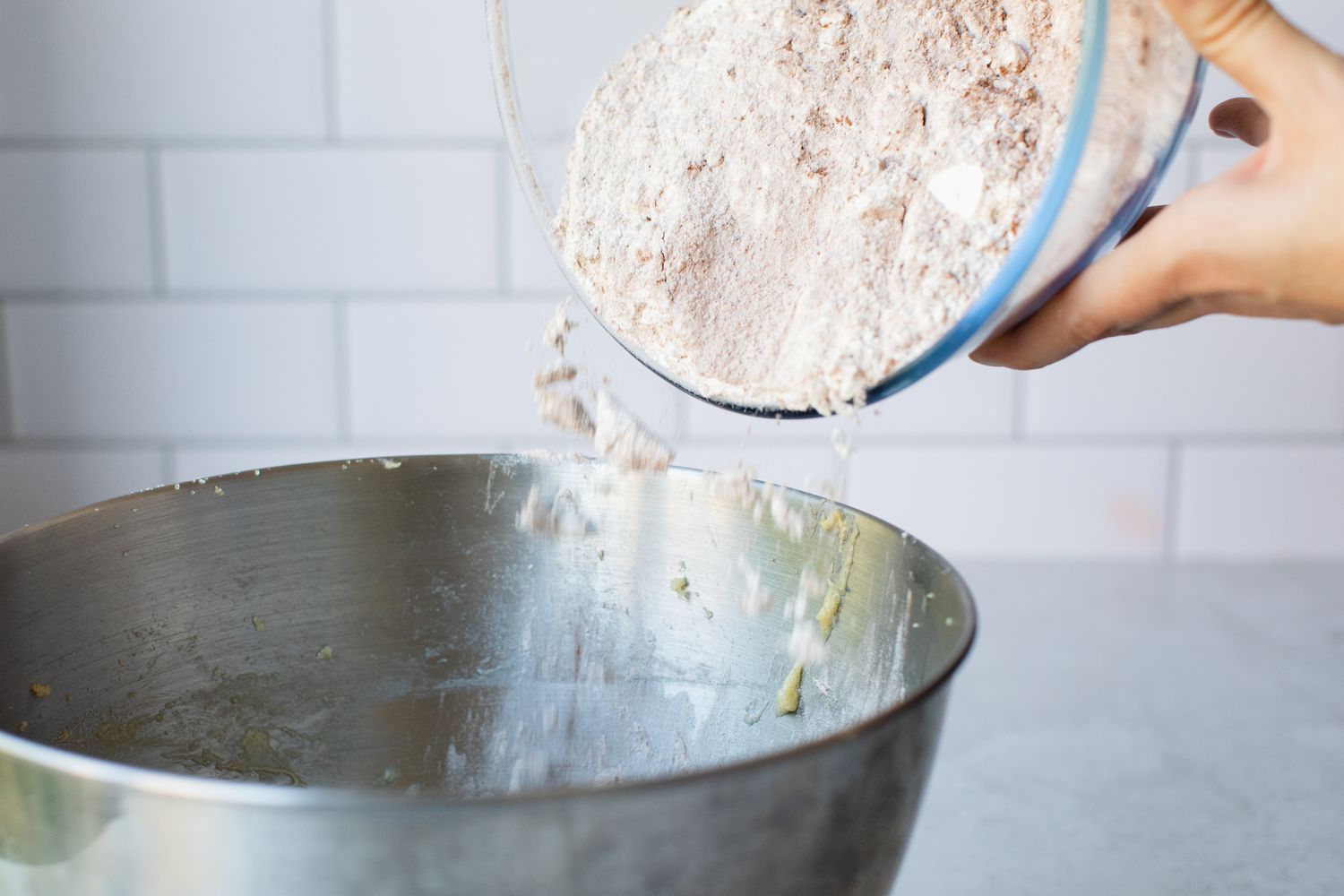 Adding dry ingredients to a stand mixer bowl for a red velvet cupcake recipe.