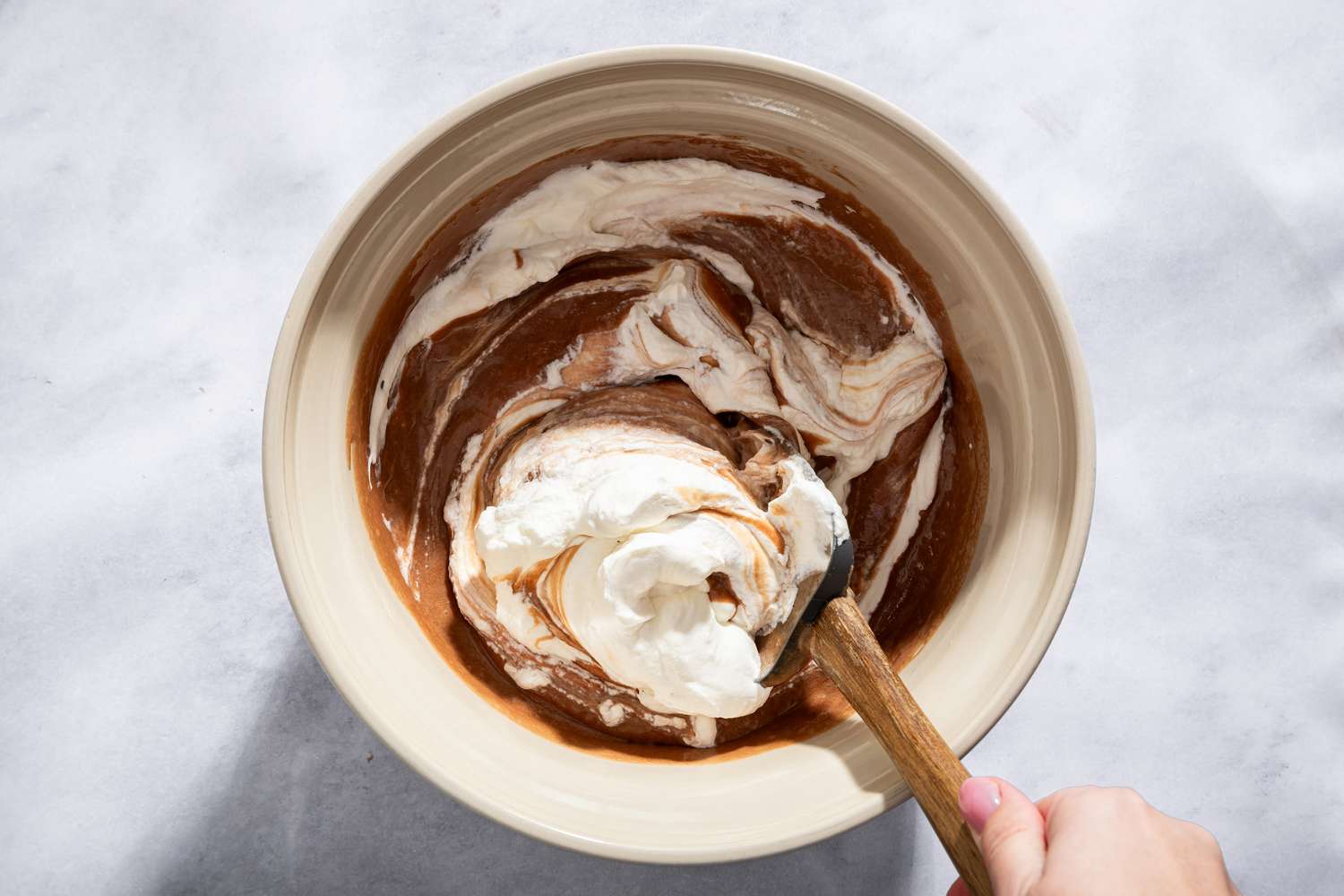 A person mixing creamy ingredients in a bowl with a wooden spoon