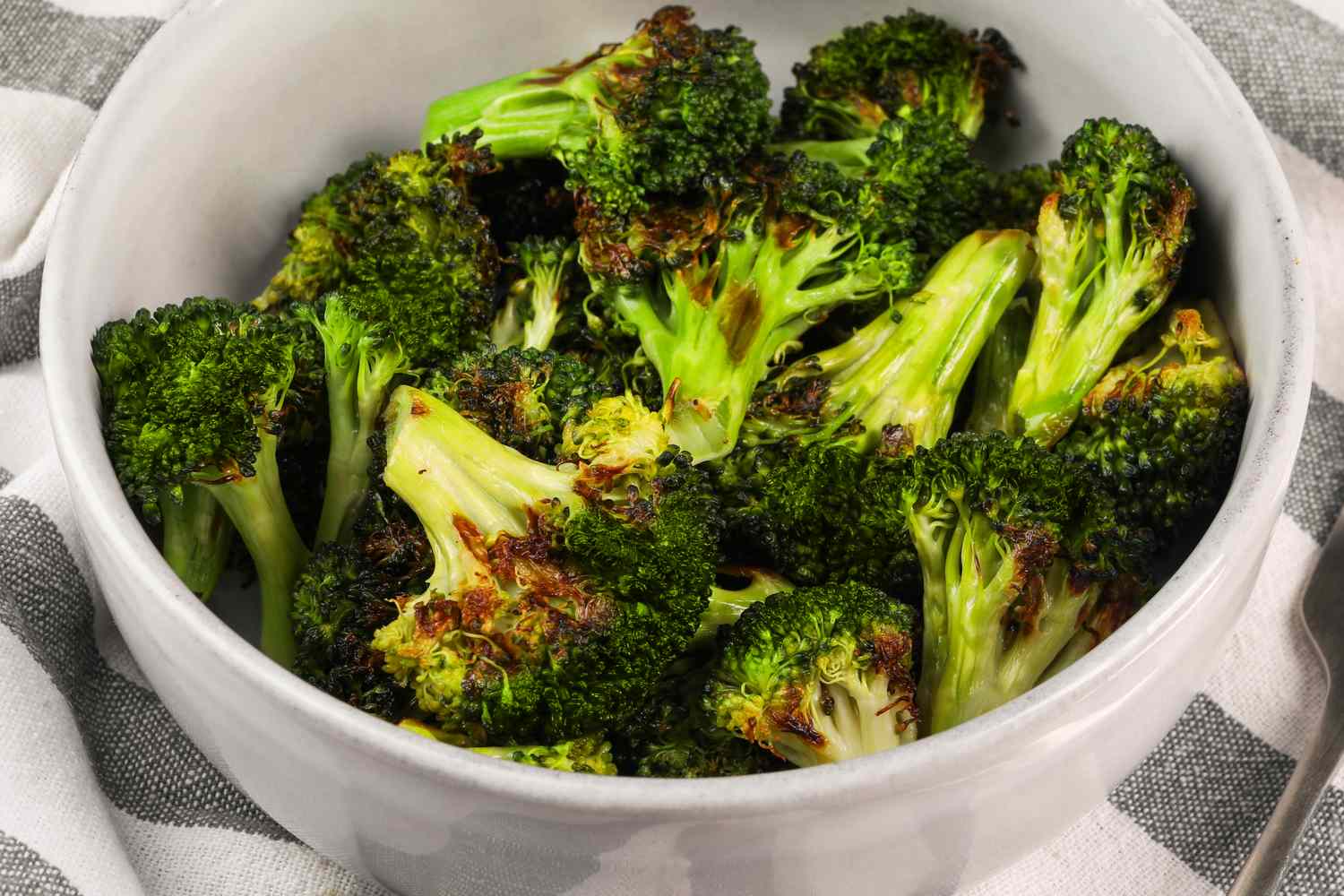 A bowl with roasted broccoli pieces on a checkered tablecloth