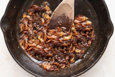A wooden spoon stirring caramelized onions in a cast iron skillet to show how to make caramelized onions.
