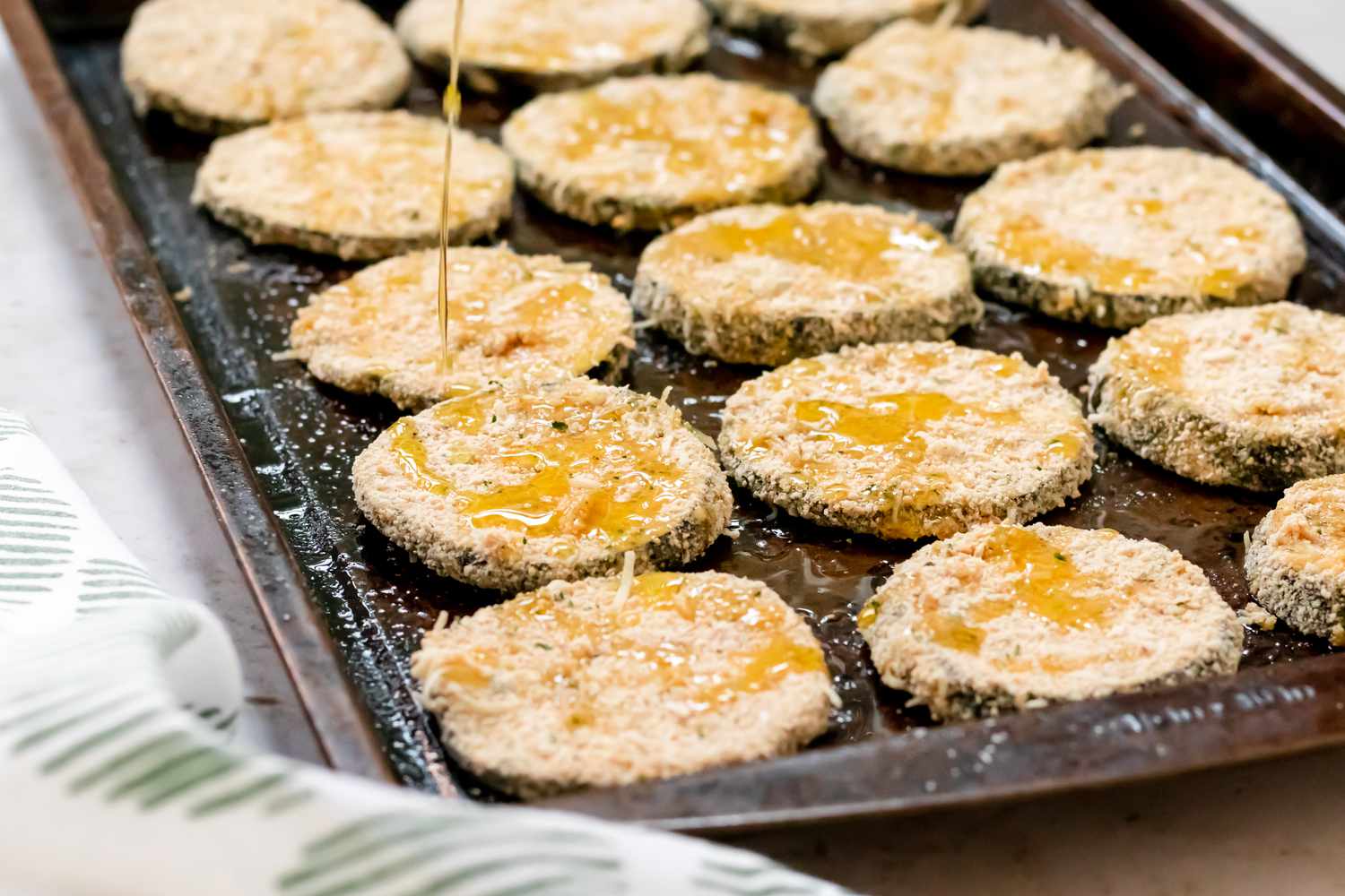 Drizzling oil over breaded eggplant on a baking dish