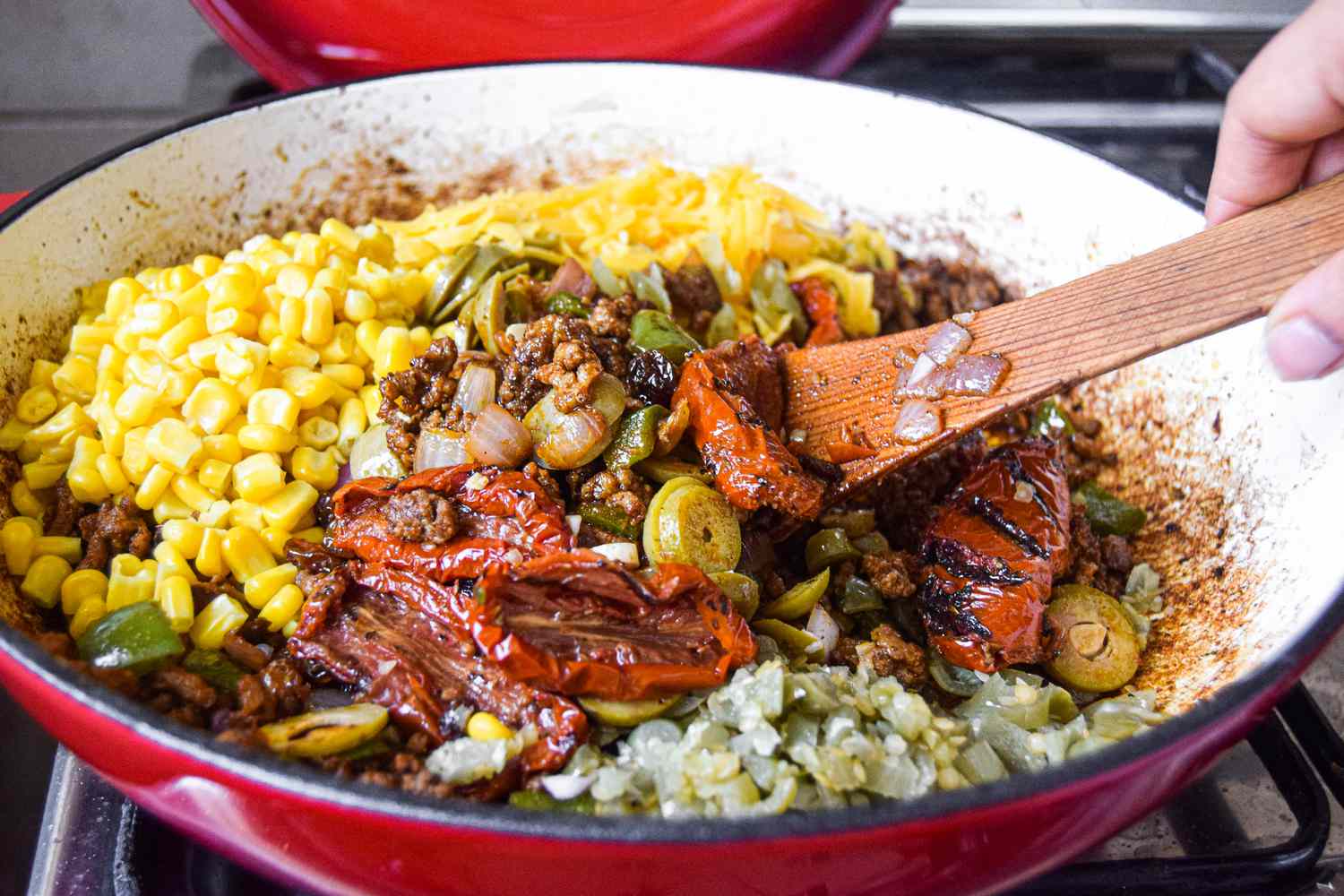 Corn, peppers, and other ingredients being stirred into the ground beef mixture