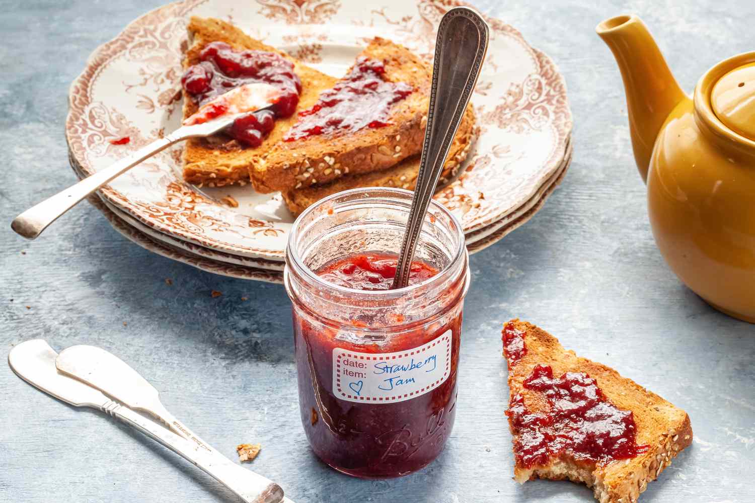 Strawberry Jam Surrounded by Toast on Plate, Utensils, and Tea Pot on Table