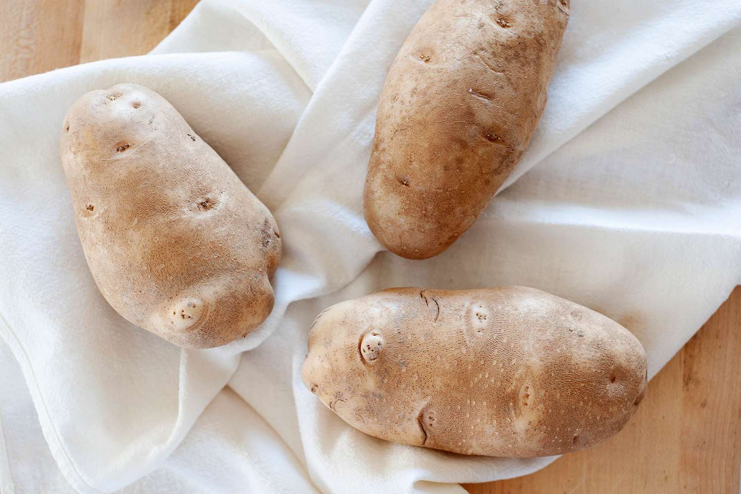 Three russett potatoes on a white linen.