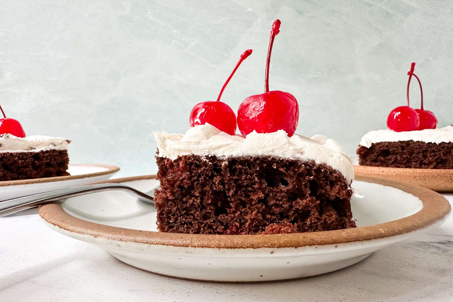 Chocolate cake slice on a plate topped with white frosting and cherries