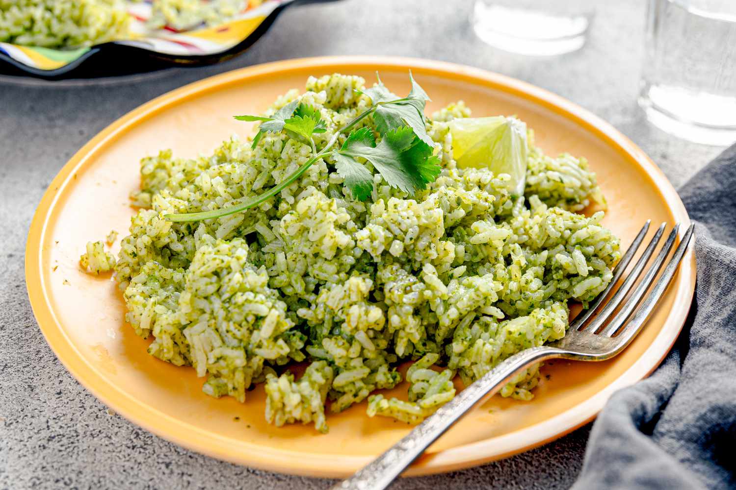 Microwave Arroz Verde on a Plate with a Fork Next to a Table Napkin, Glasses of Water, and a Plate with More