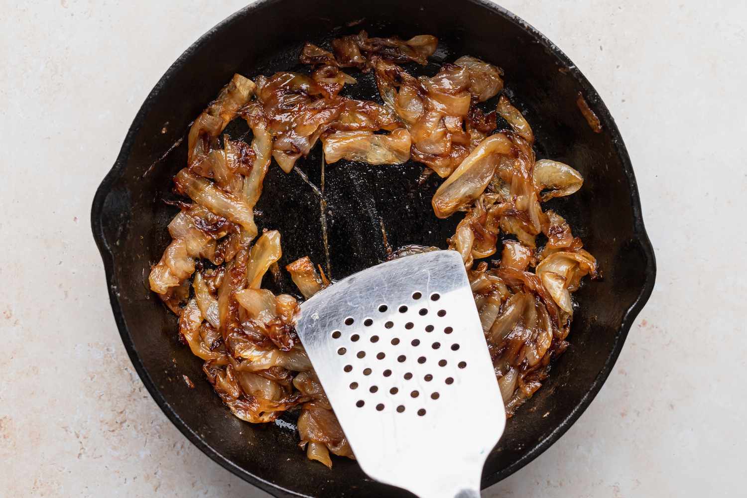 A metal spatula scrapping browned onions off the surface of a cast iron skillet